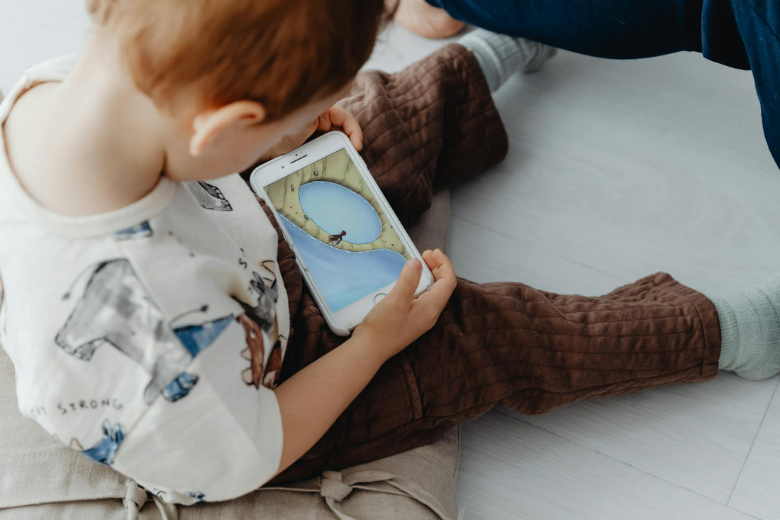 bambino piccolo seduto a terra che guarda un cartone animato sullo smartphone, uso precoce di schermi invece di giochi fisici