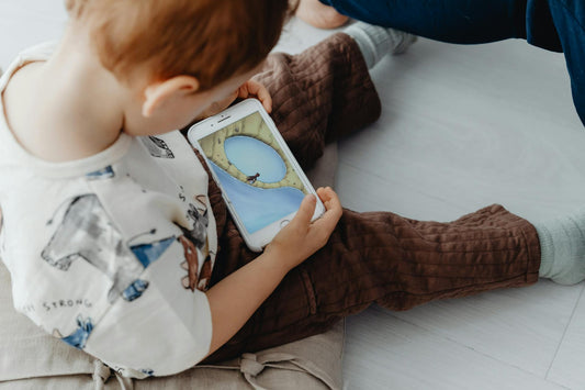 bambino piccolo seduto a terra che guarda un cartone animato sullo smartphone, uso precoce di schermi invece di giochi fisici